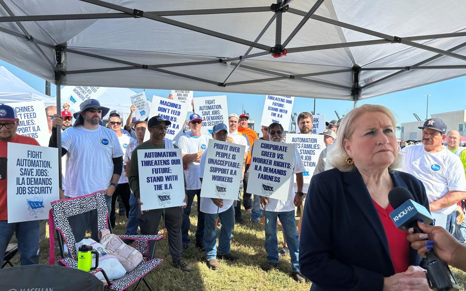 Congresswoman Sylvia Garcia is interviewed by KHOU in the right of the frame. Behind her is a line of striking longshoremen holding signs about fighting automation, putting people over profits.